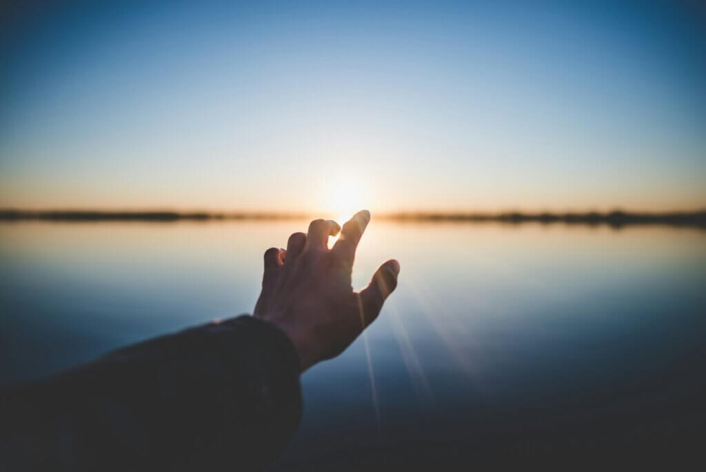 Hand zeigt richtung Sonne als Symbol für die Hoffnung